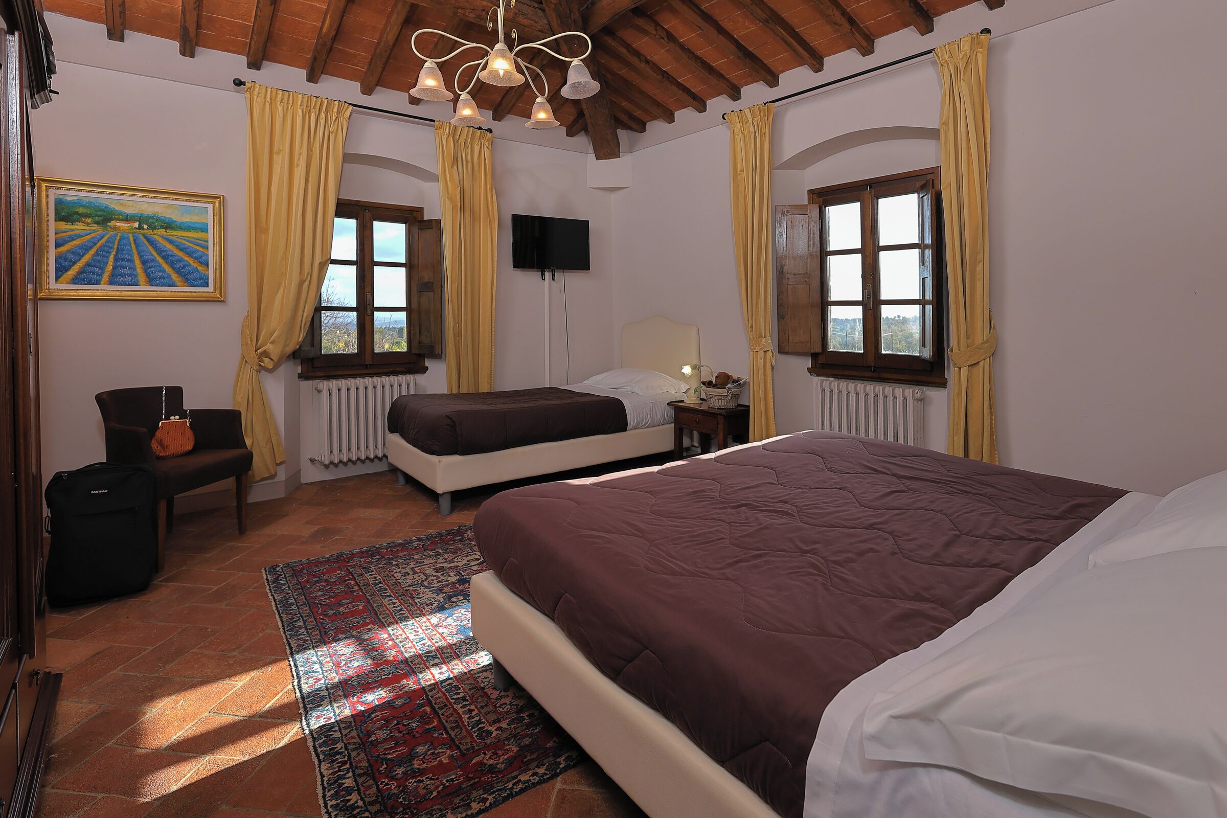 A bedroom with a large bed, a television, and a painting of a vineyard on the wall.