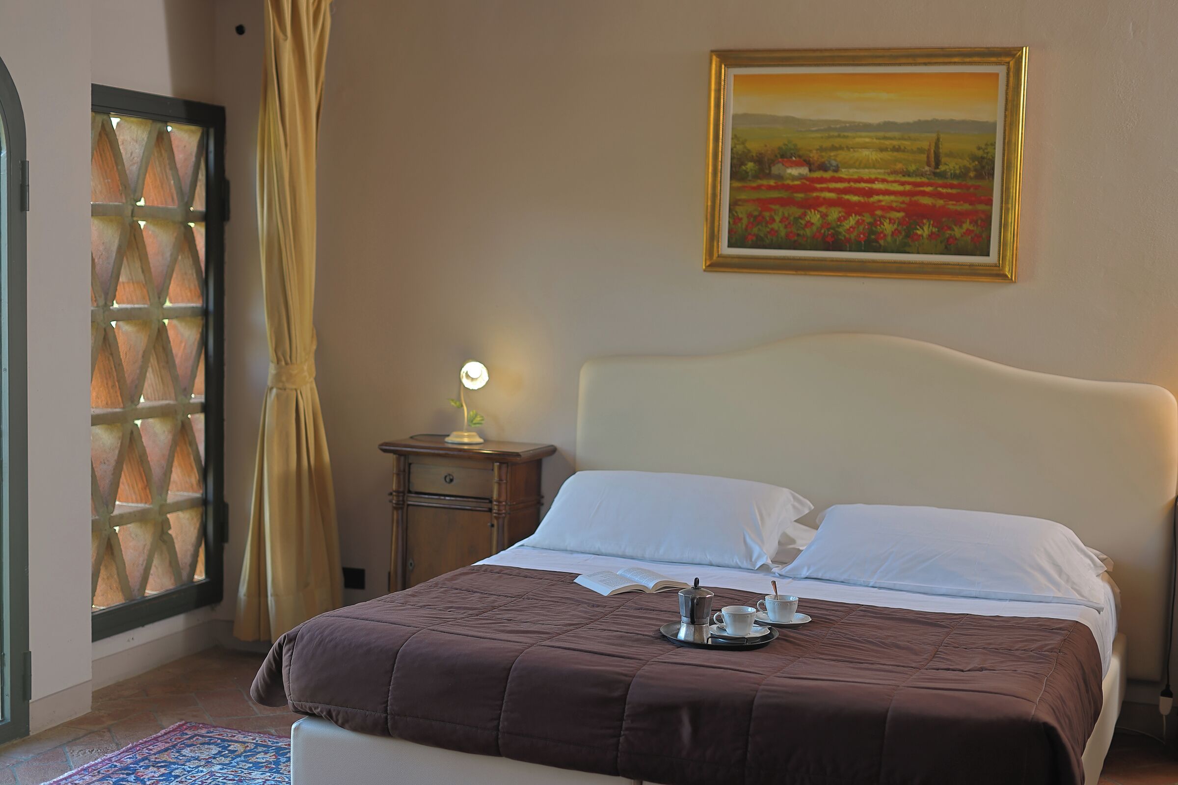 A neatly made bed with a brown bedspread, a bedside table with a lamp, and a painting on the wall.