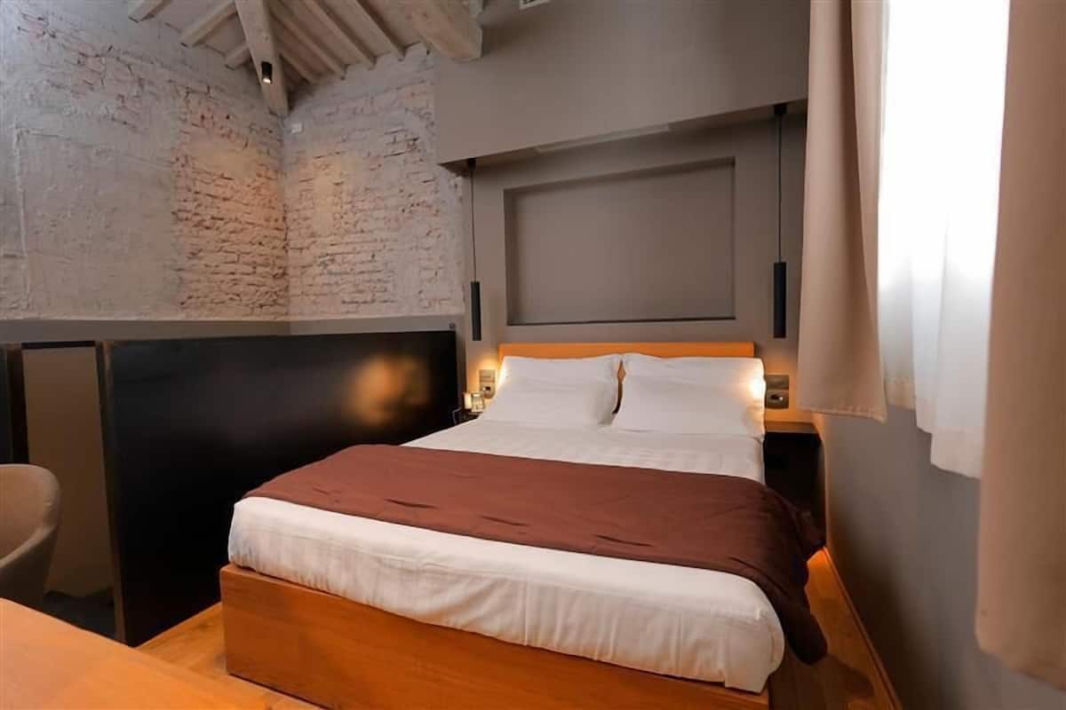 Ein Schlafzimmer mit Backsteinwand, hölzernem Bettgestell, Kopfteil und Nachttisch mit Lampe.