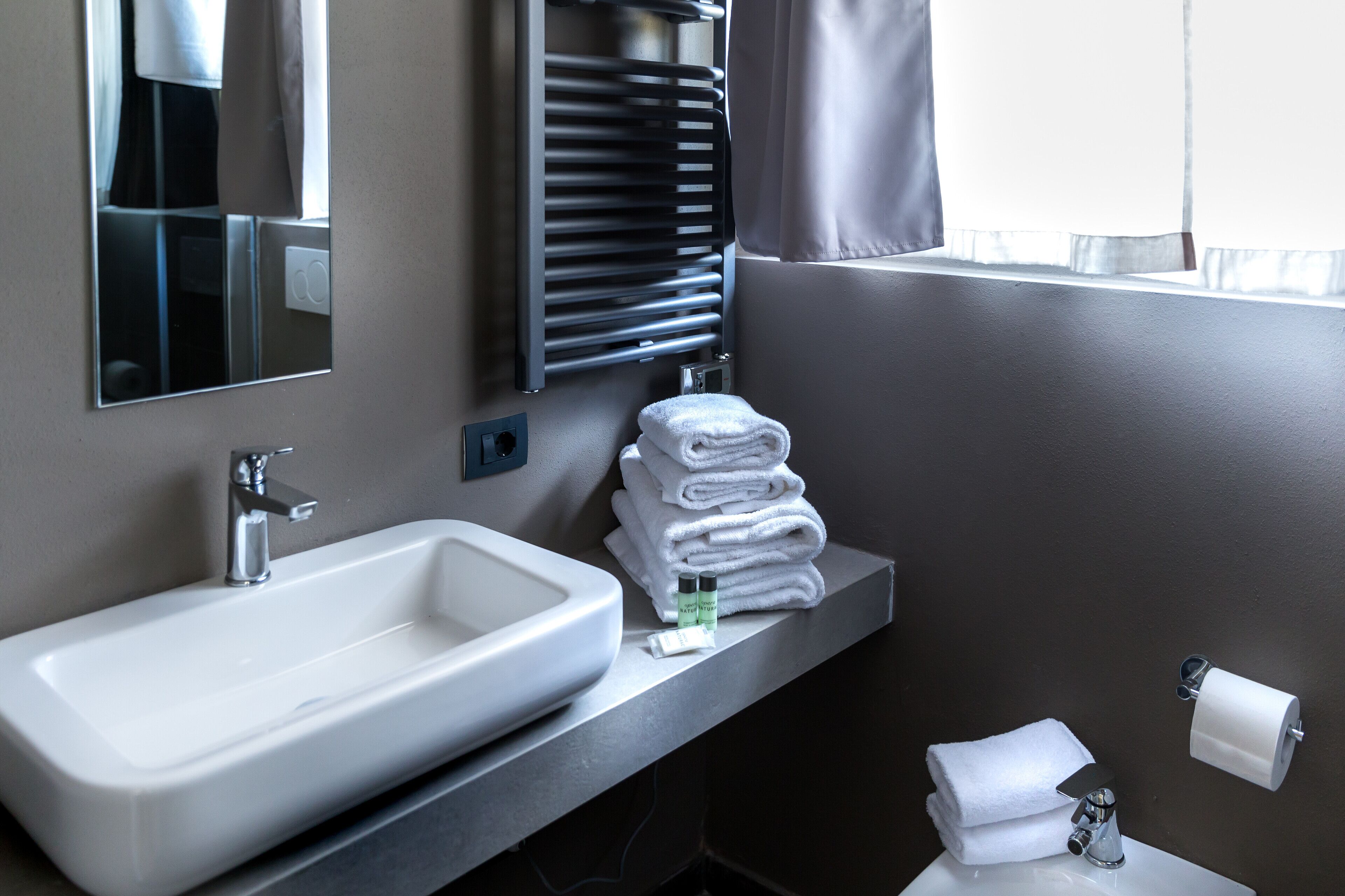 Un baño con lavamanos, espejo, toallero y dispensador de papel higiénico.