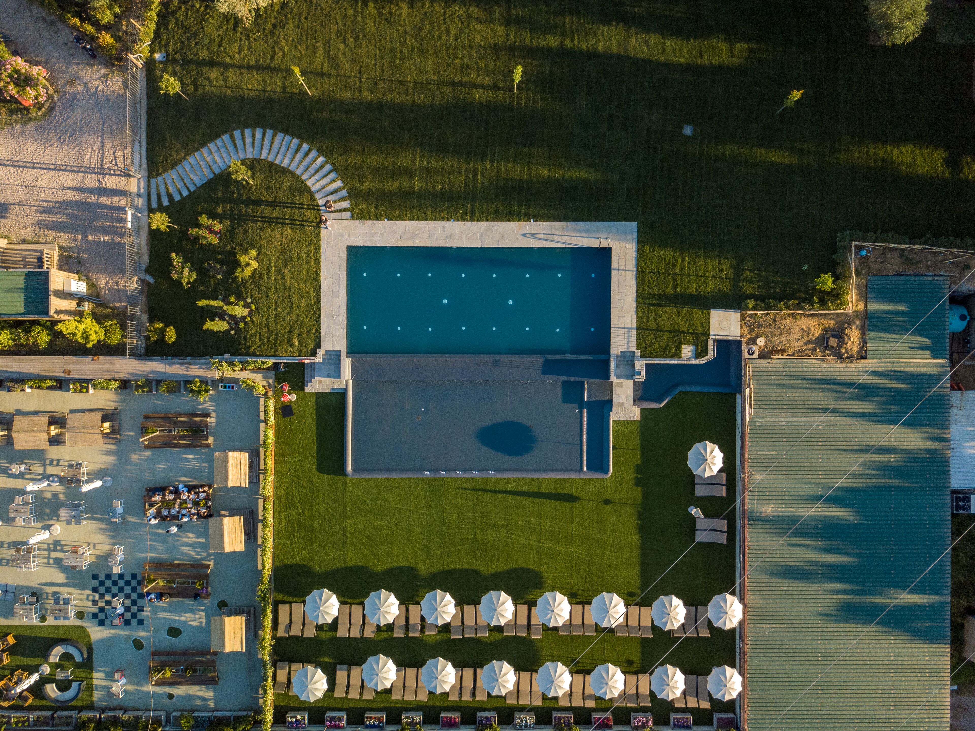 An aerial view of a resort with a swimming pool, outdoor seating, and a parking area.