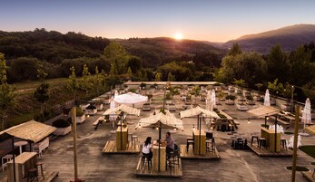 Un área de comedor al aire libre con varias mesas y sombrillas, rodeada de vegetación y colinas al fondo.