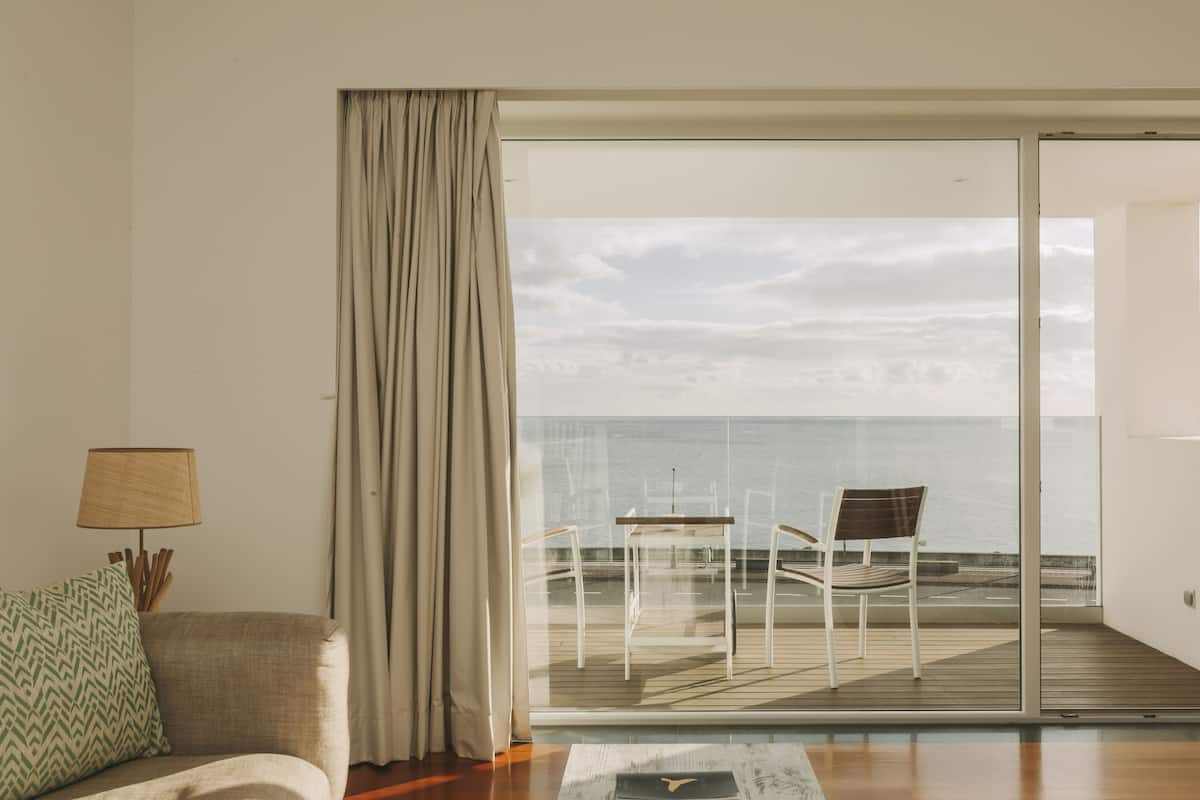 Habitación con vista al mar a través de un ventanal, un sofá, una lámpara y una silla en una terraza.