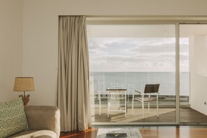 Habitación con vista al mar a través de un ventanal, un sofá, una lámpara y una silla en una terraza.