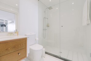 Un baño moderno con cabina de ducha de vidrio, inodoro blanco y tocador de madera con espejo.