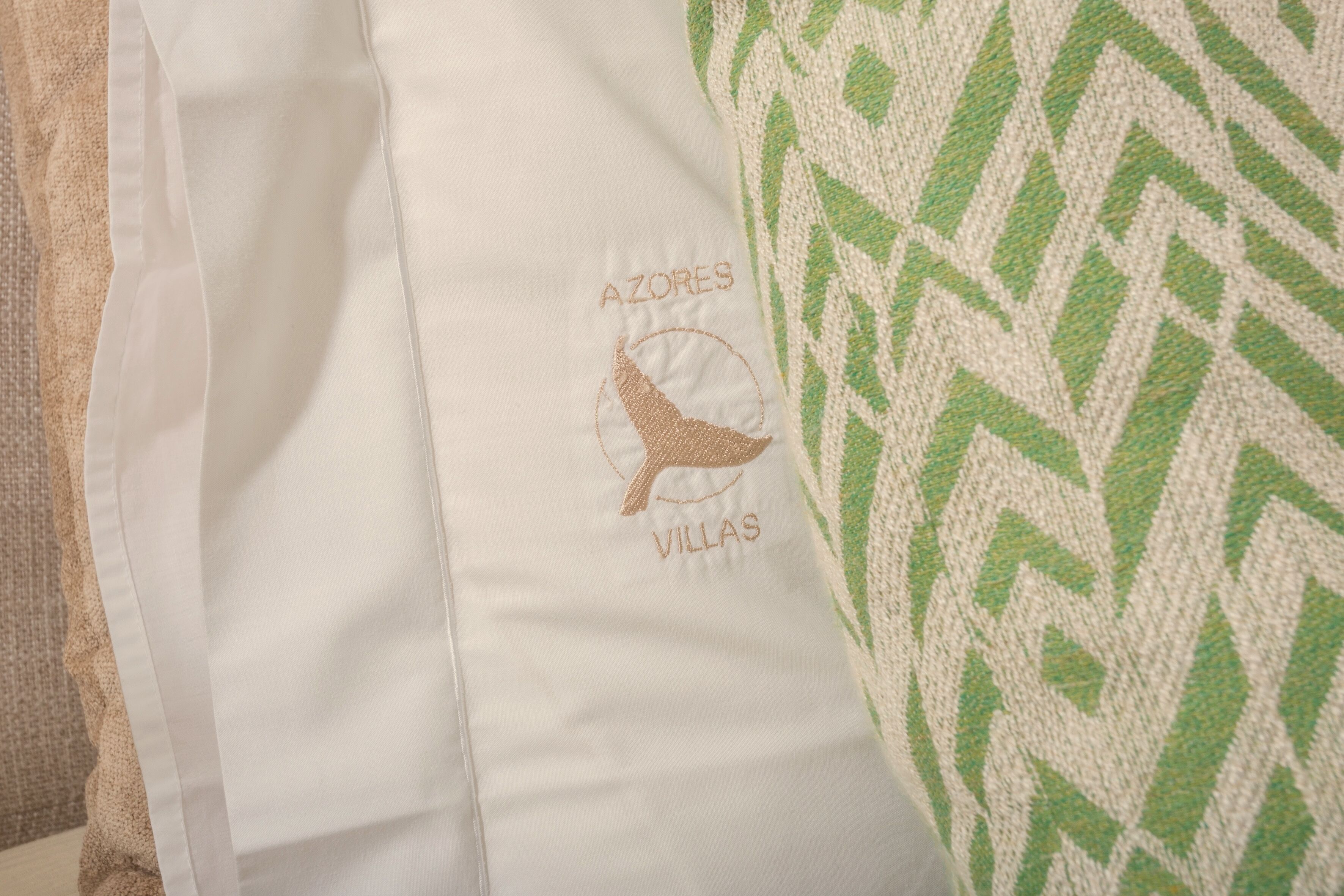 A white pillow with embroidered text and a logo, and a green patterned pillow.