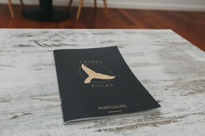 Un folleto negro con el título "AZORES VILLAS PORTUGUES" sobre una mesa de madera rústica.