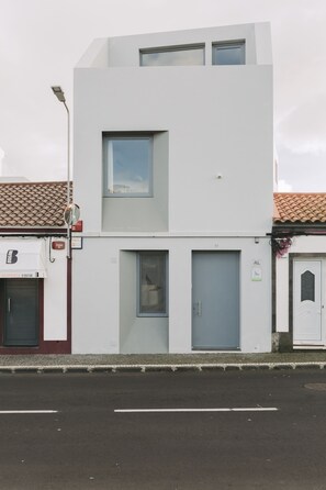 Un edificio moderno de dos pisos con fachada plana, un ventanal en el nivel superior y una puerta en la planta baja.