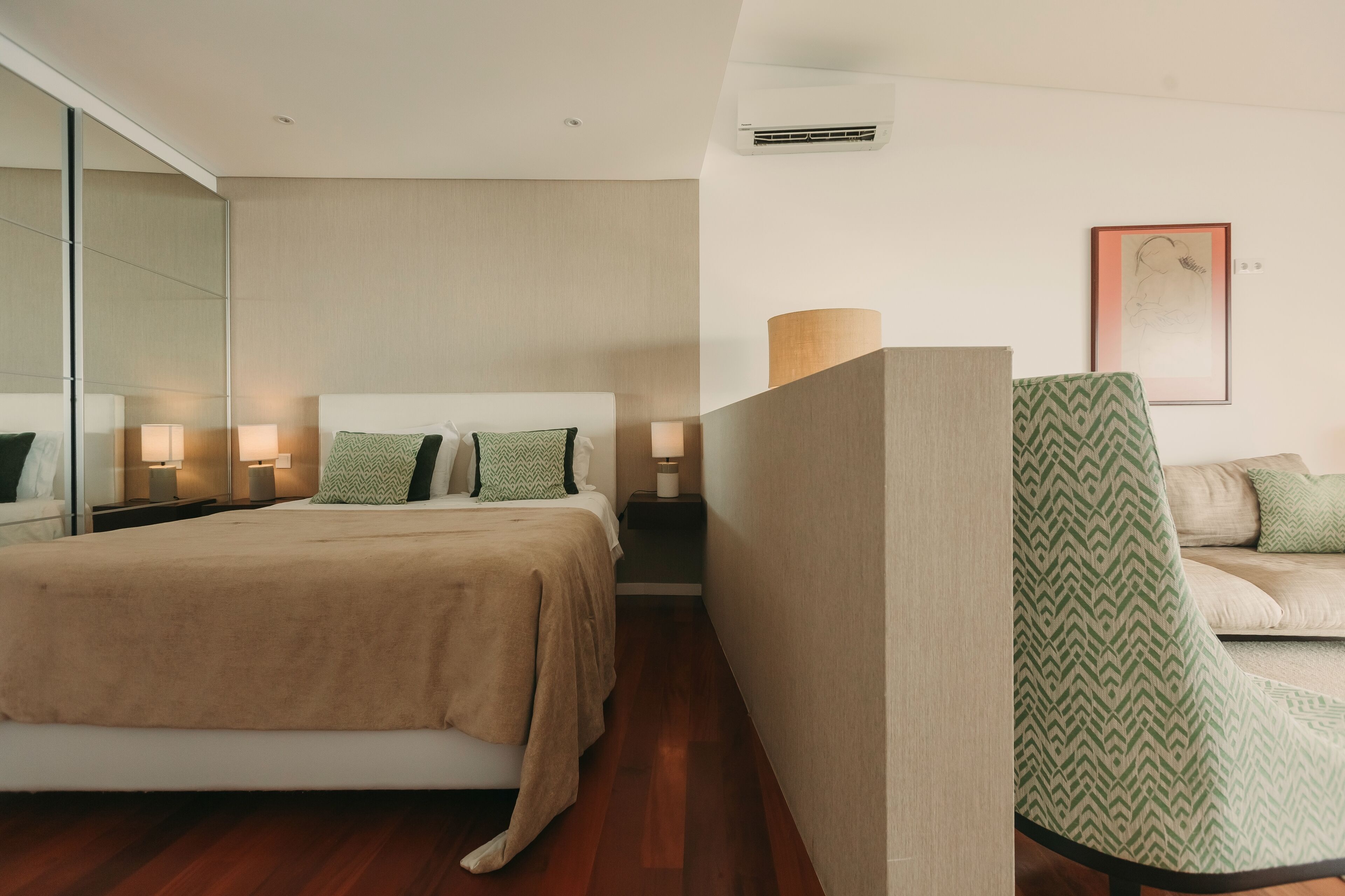A modern hotel room with a large bed, bedside lamps, a sofa, and a mirror.