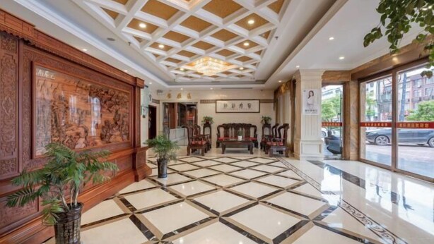 A lobby with a tiled floor, wooden paneling, a chandelier, and a large window. - Xingji Hotel (Dongyang)