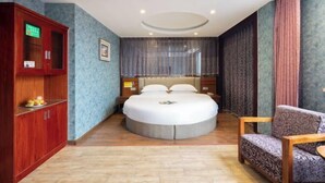 A hotel room with a round bed, a wooden cabinet, a chair, and a window with curtains. - Xingji Hotel (Dongyang)