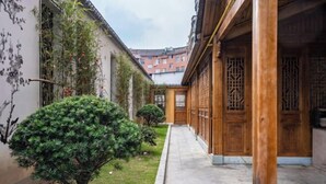 A narrow corridor with a wooden door, a small tree, and a wall with a mural. - Xingji Hotel (Dongyang)