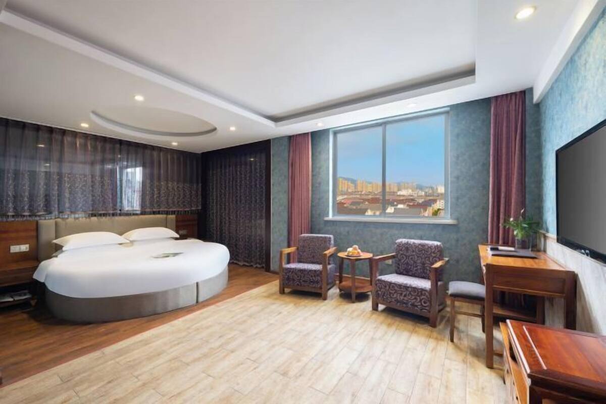 A modern hotel room with a large bed, two armchairs, a small table, and a TV.