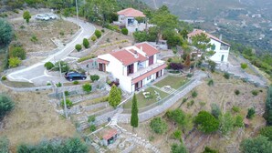 Uma casa de dois andares com telhado vermelho, um pequeno jardim e uma estrada sinuosa nas proximidades.