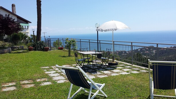 Um pátio com mesa e cadeiras, um guarda-sol branco e uma vista panorâmica do oceano.