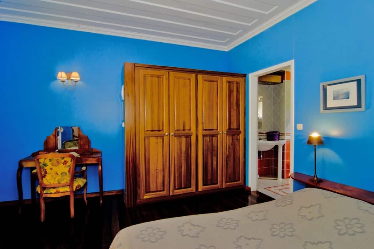 Habitación con paredes azules, un armario de madera, un escritorio con una silla y una cama con colcha estampada.