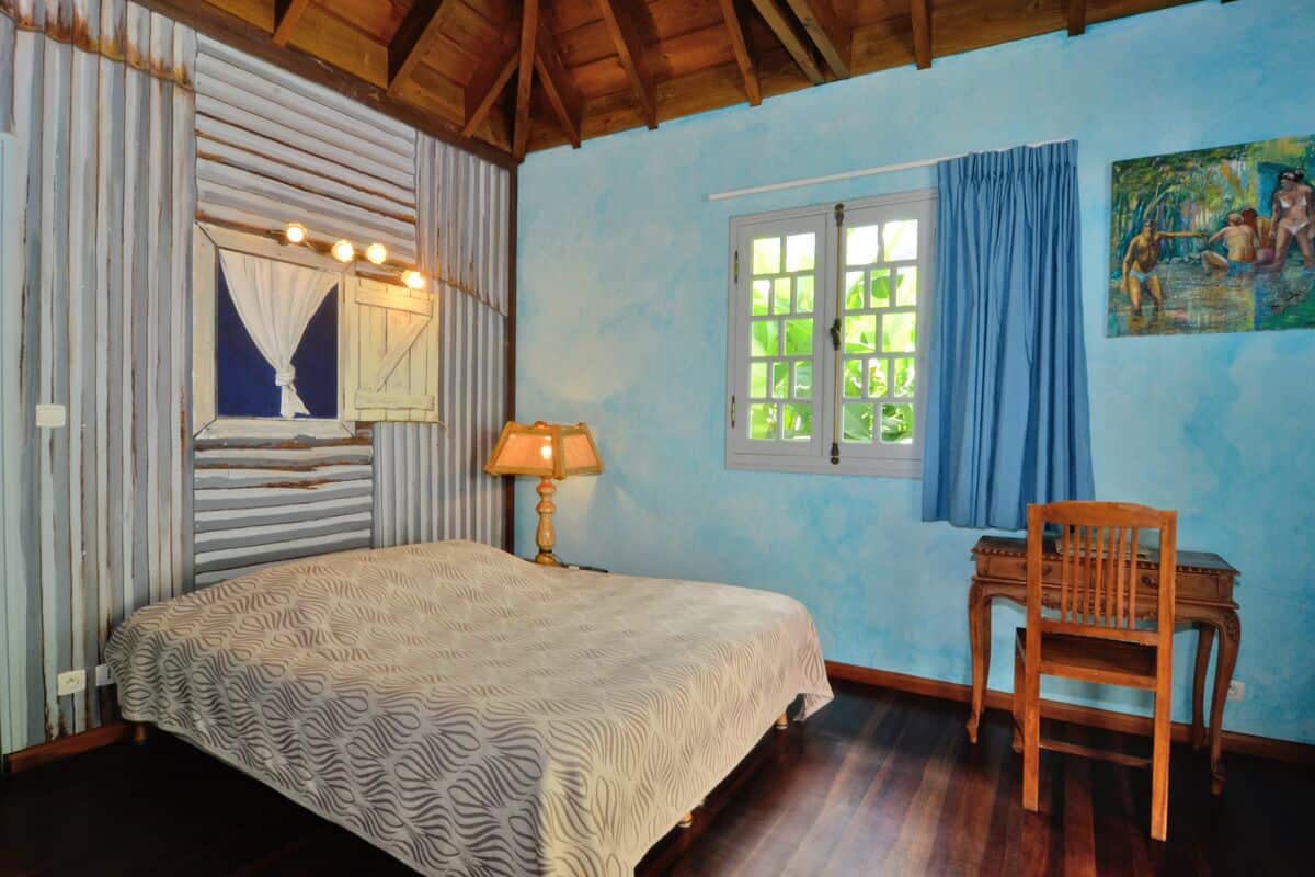 Un dormitorio con cama, una silla, una ventana con cortinas y un cuadro en la pared.