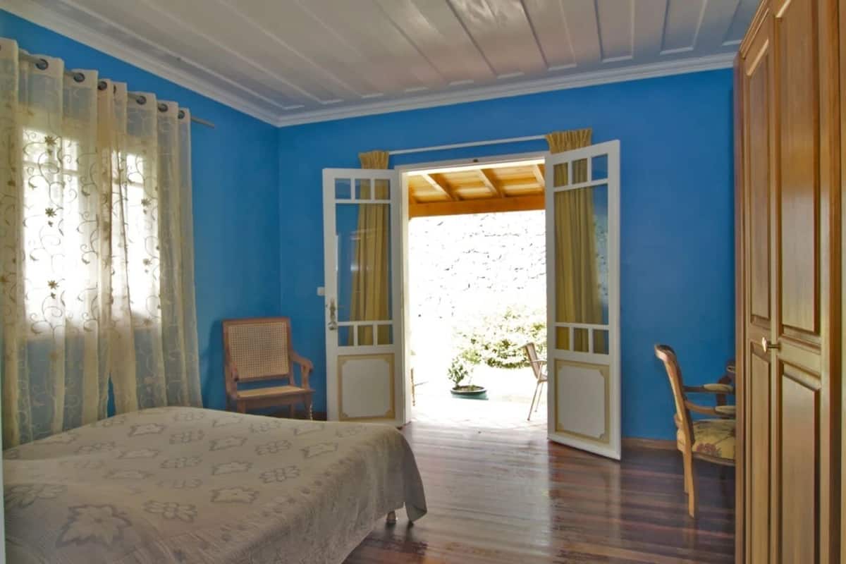 Un dormitorio con una cama, una silla y una puerta abierta que da al exterior.