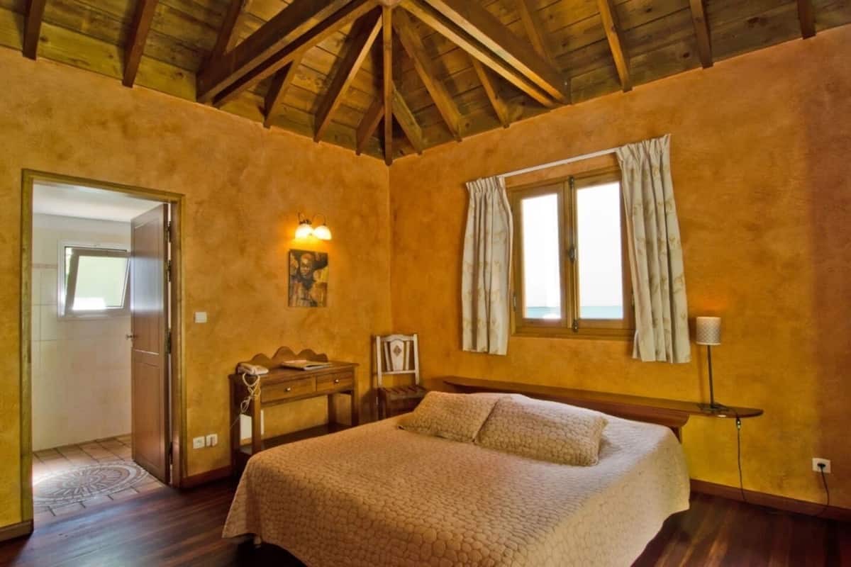 Un dormitorio con cama, escritorio, silla, lámpara y ventana con cortinas.