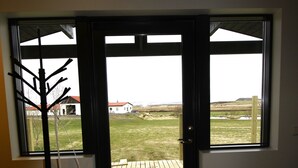 Una habitación con piso de madera, una puerta negra y vista a un área verde exterior.