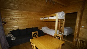 Una habitación de cabaña de madera con literas, un sofá, una mesa y un taburete pequeño.