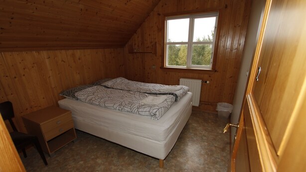 Una habitació amb panells de fusta, un llit, un escriptori petit i una finestra.