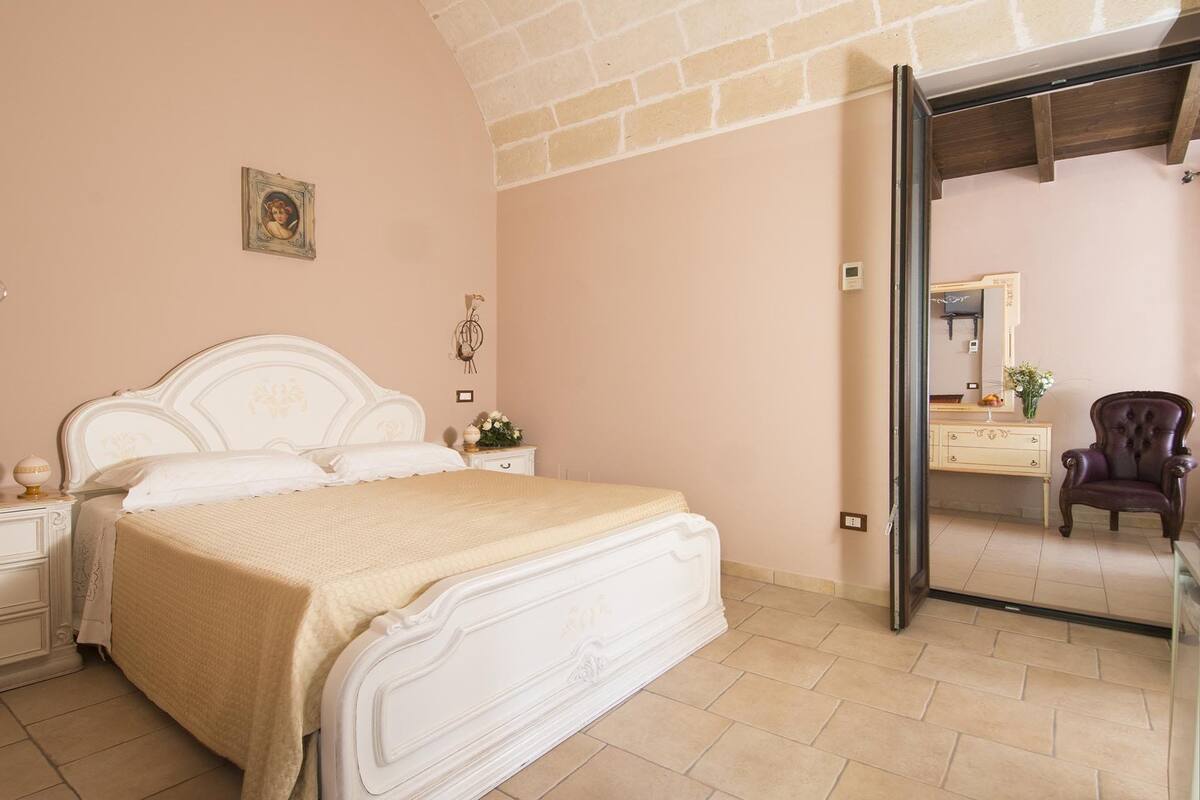 Une chambre à coucher avec un lit blanc, une table de chevet, une commode, une chaise et un miroir.
