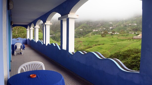 Un balcón techado con vistas a un paisaje verde y casas a lo lejos.