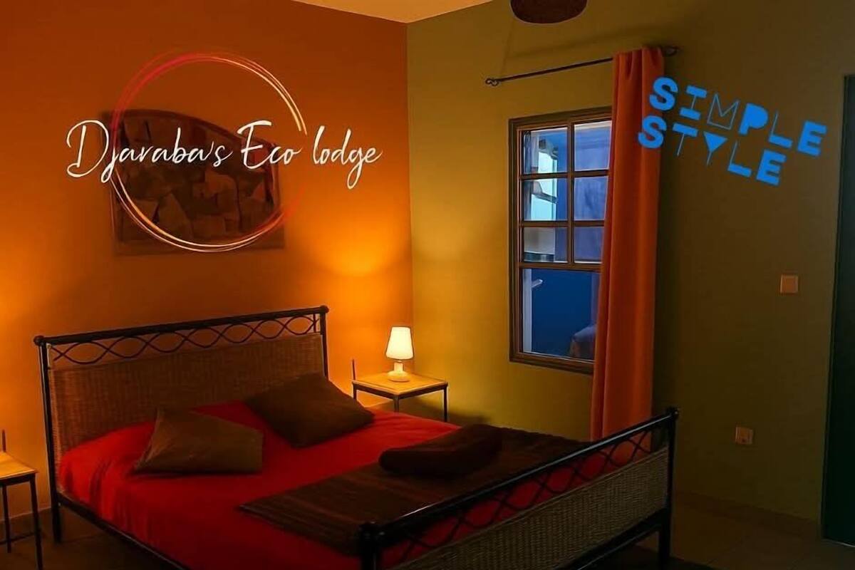 Una habitación con cama, mesita de noche, lámpara y ventana con cortinas.