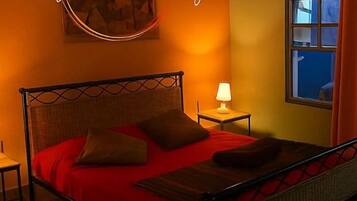 Una habitación con cama, mesita de noche, lámpara y ventana con cortinas.