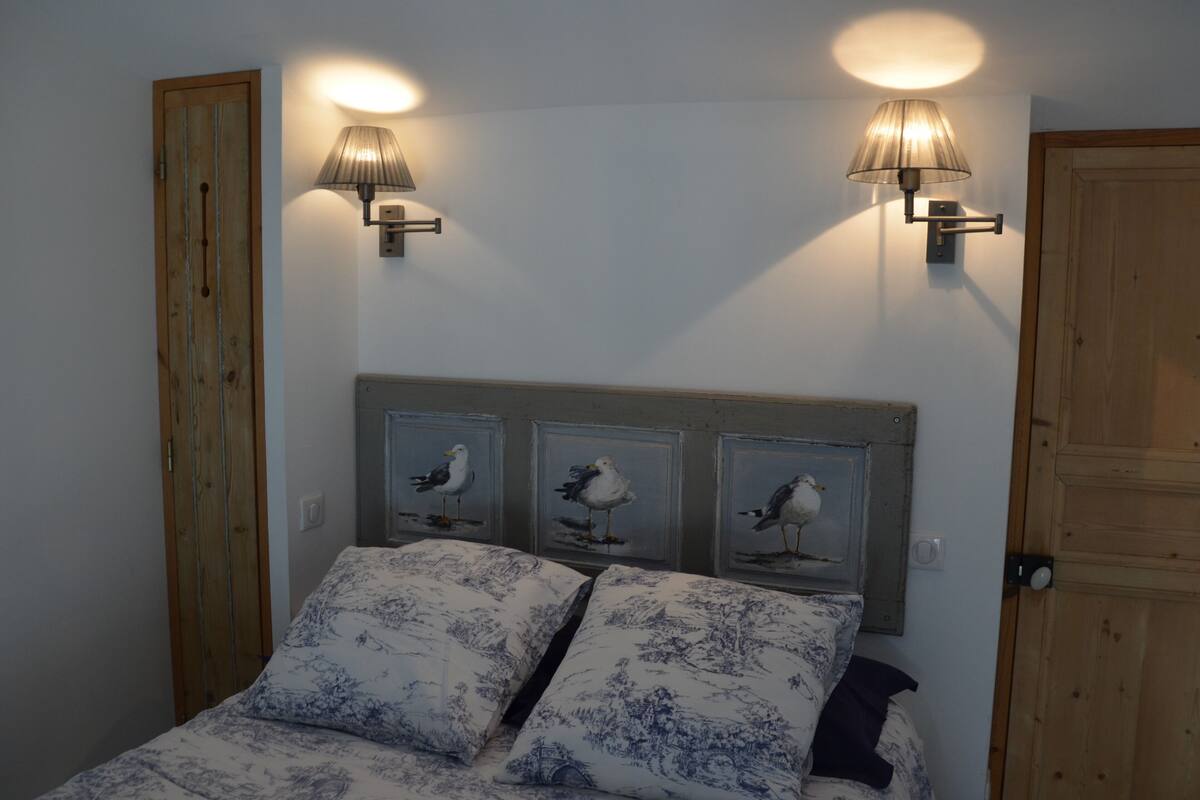 A bedroom with a bed, two wall-mounted lamps, and three framed pictures of birds on the headboard.