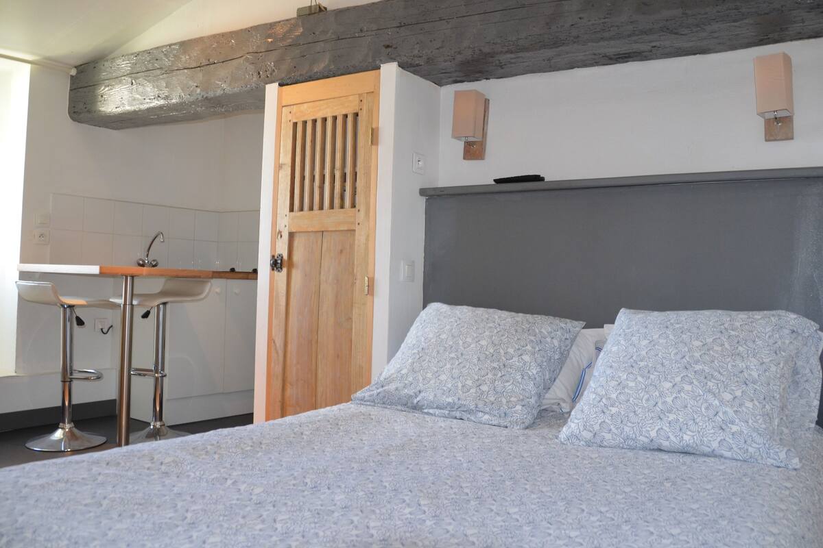 A bedroom with a bed, a wooden door, a bathroom with a sink, and a bar area.