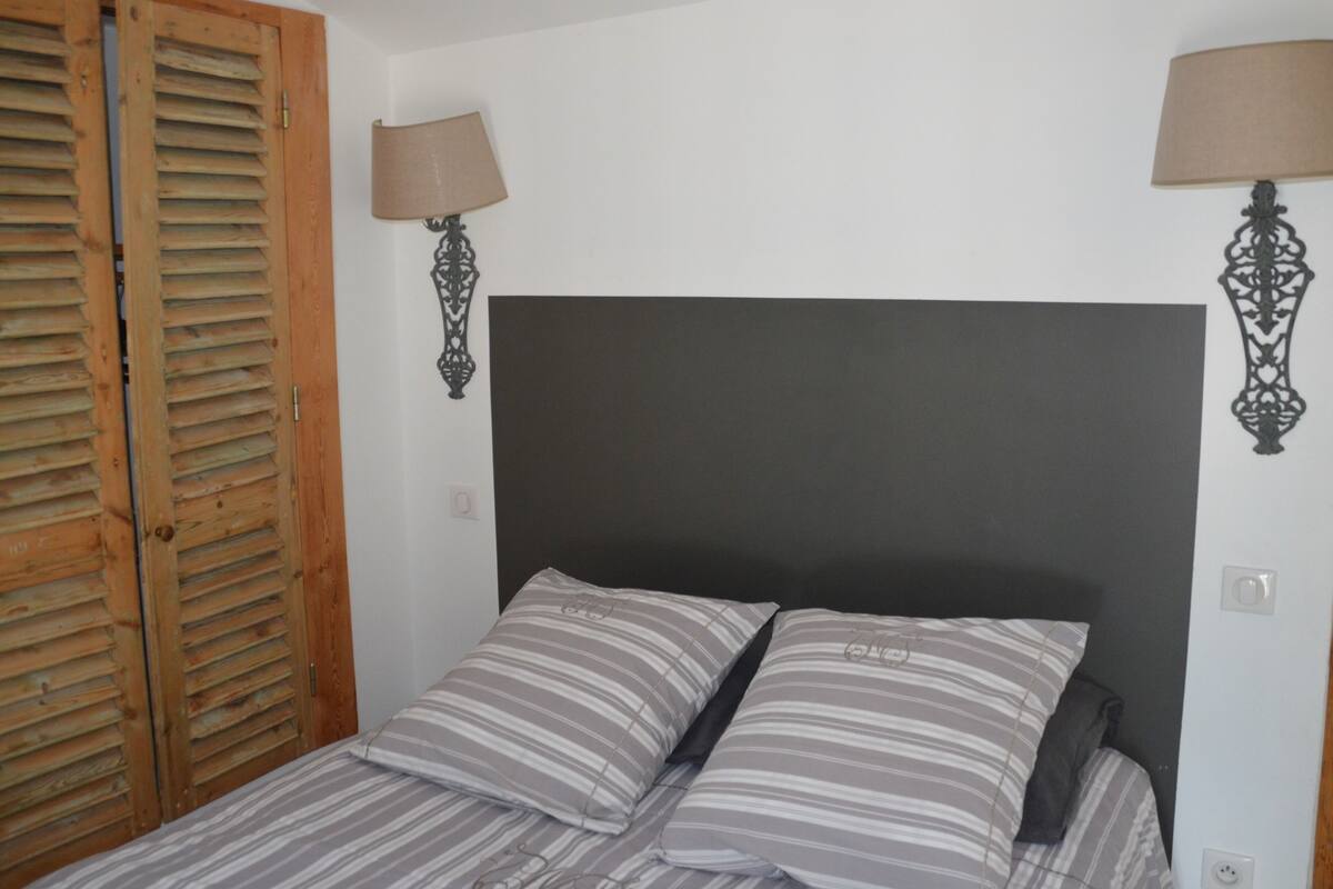 A bedroom with a bed, two pillows, a wooden door, and two wall-mounted lamps.