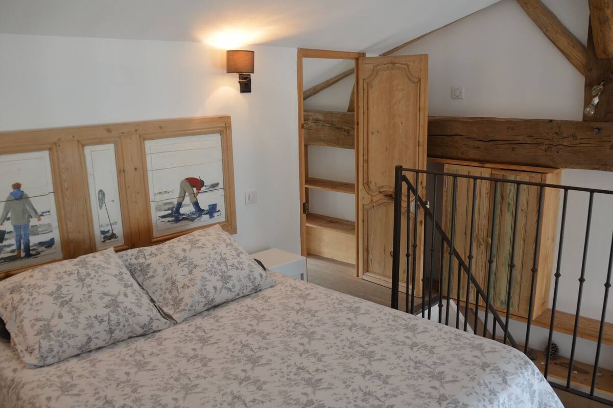 A bedroom with a bed, a wooden staircase, and a wall-mounted lamp.