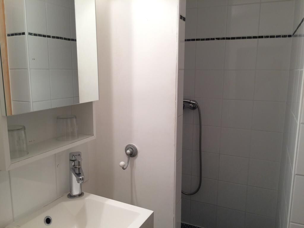 Une salle de bain avec un lavabo blanc, un miroir et un espace douche dont les murs sont recouverts de carreaux.
