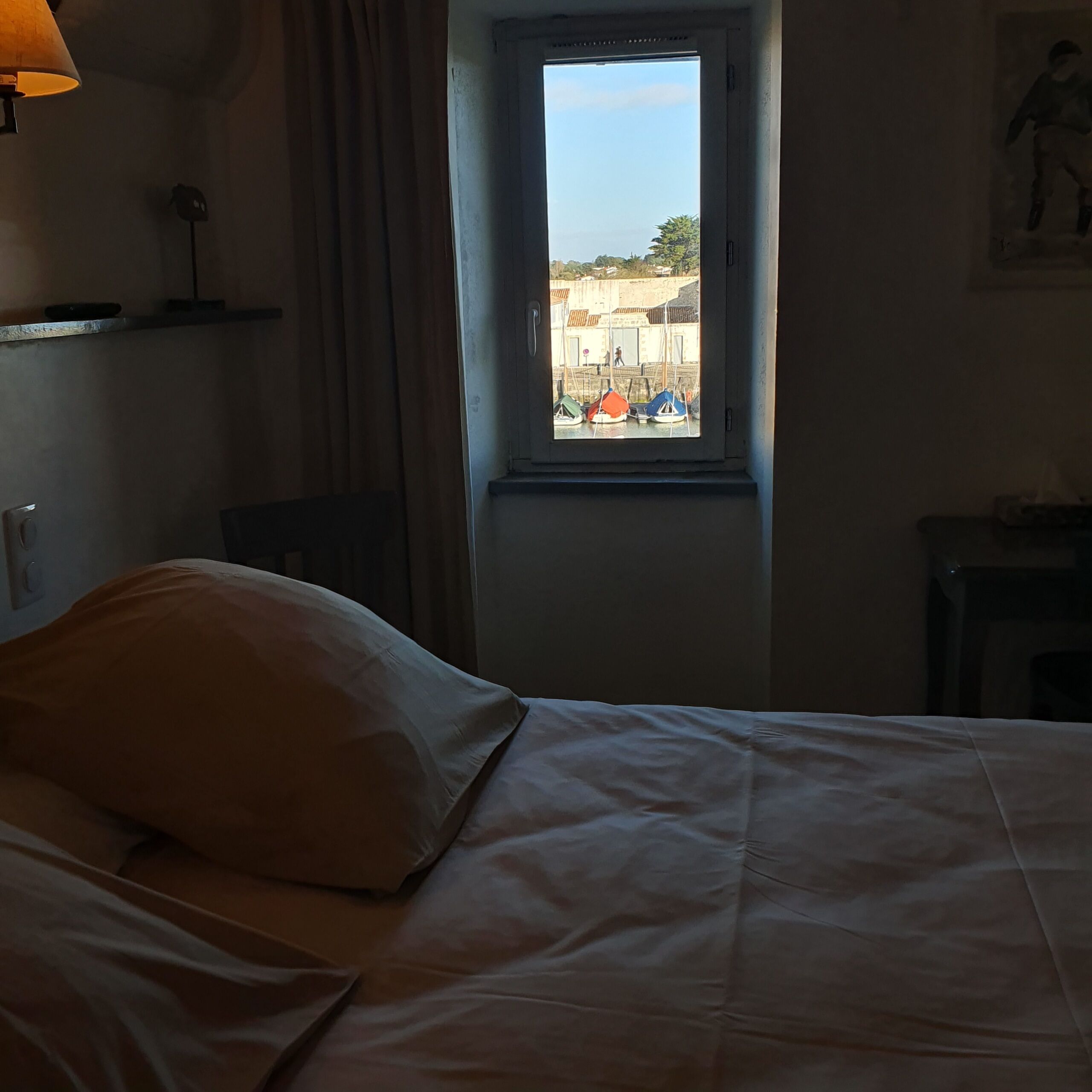 Et hotelværelse med en seng, et vindue og udsigt til både og bygninger udenfor.