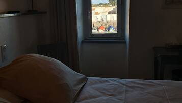 A hotel room with a bed, a window, and a view of boats and buildings outside.