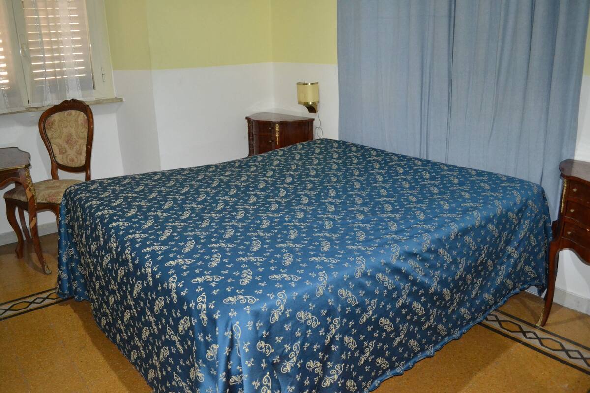 A bedroom with a bed, a chair, a nightstand, and a lamp.