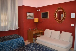 A room with a red wall, a white sofa, a wooden desk with a lamp, a framed picture, and a mirror. - Hotel Ferraro (Rome)