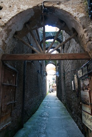 Une ruelle étroite bordée d’un mur de pierre, de poutres en bois et d’une enseigne indiquant « Tavern Allegri Ristorante ».