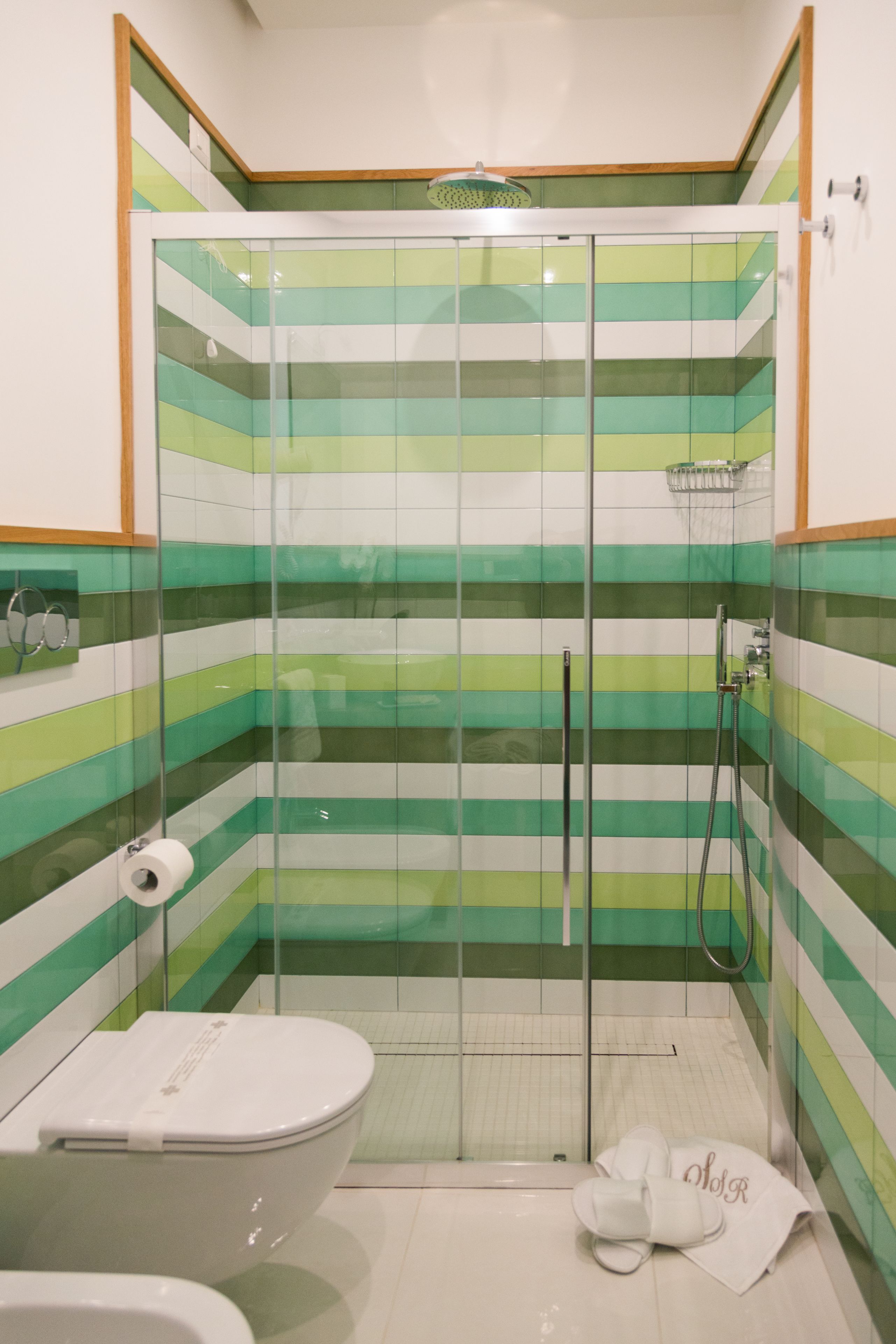 Ducha con azulejos verde y blanco a rayas, puerta de cristal y un inodoro blanco con una toalla.