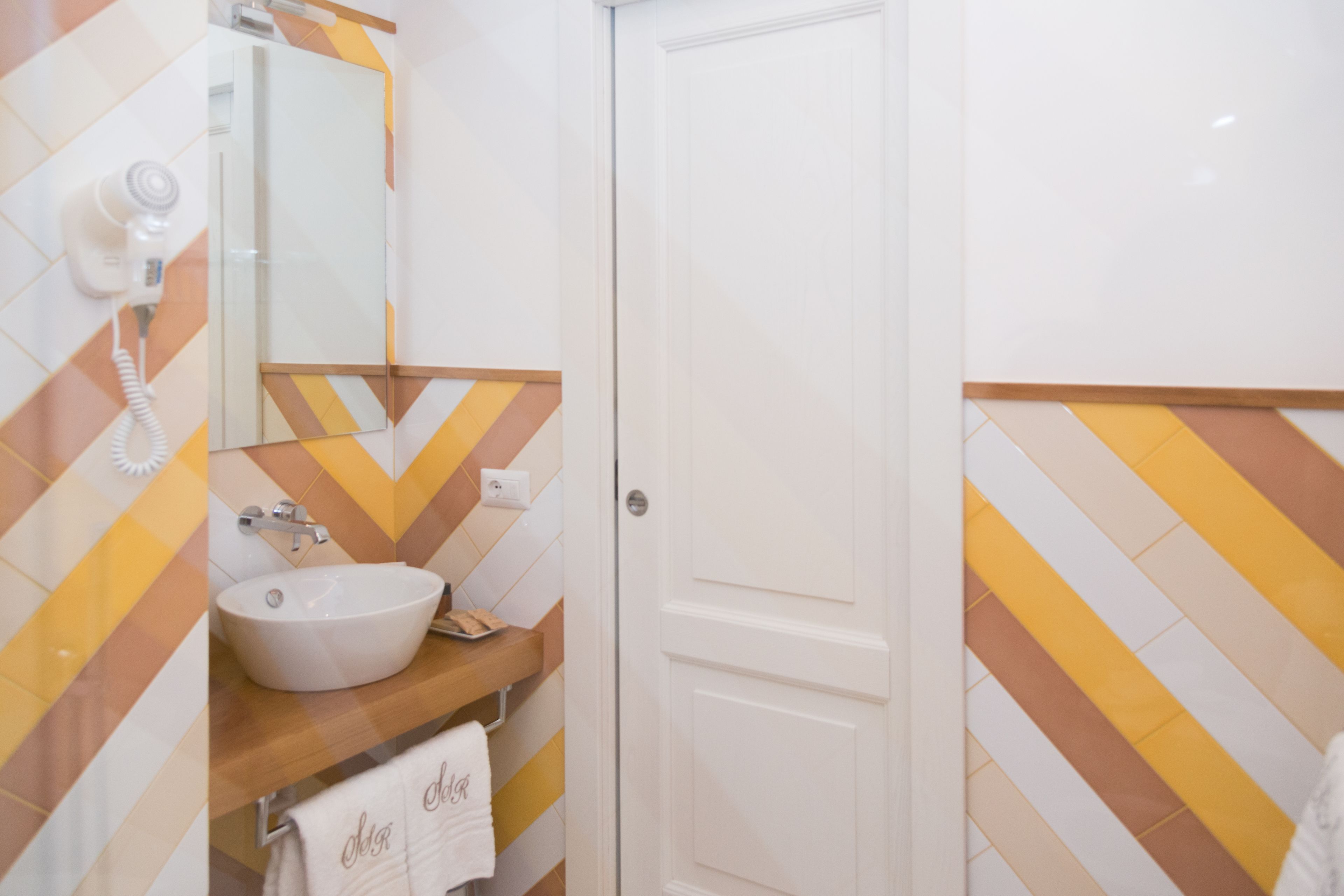 A bathroom with a white sink, mirror, and towel rack. The walls have a chevron pattern in yellow and white.