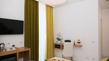 Une chambre d’hôtel avec un lit, un bureau sur lequel se trouve un plateau avec des articles pour le petit-déjeuner, un téléviseur fixé au mur et une petite plante en pot.