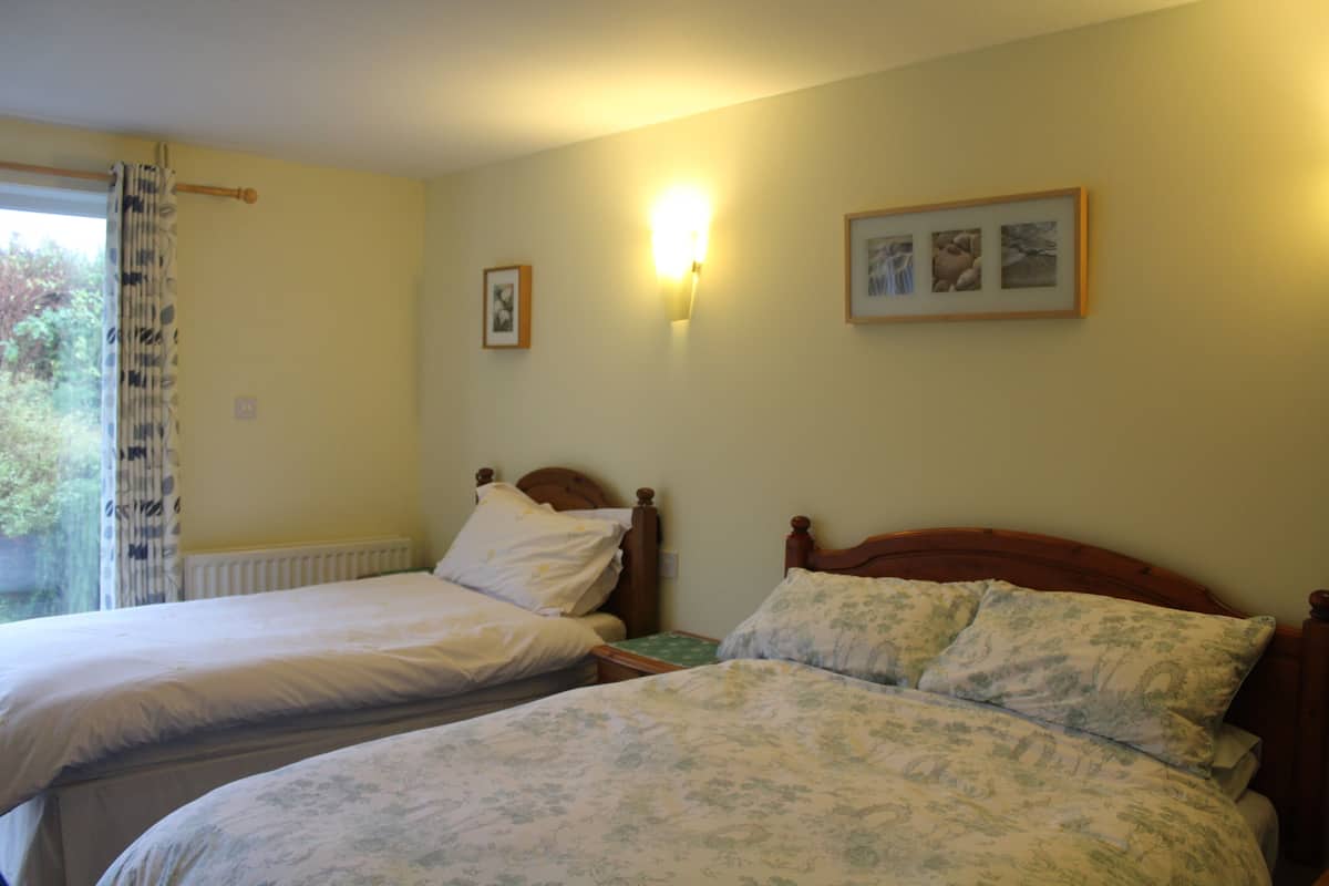 A bedroom with two single beds, a window with a curtain, a wall-mounted light, and framed pictures.