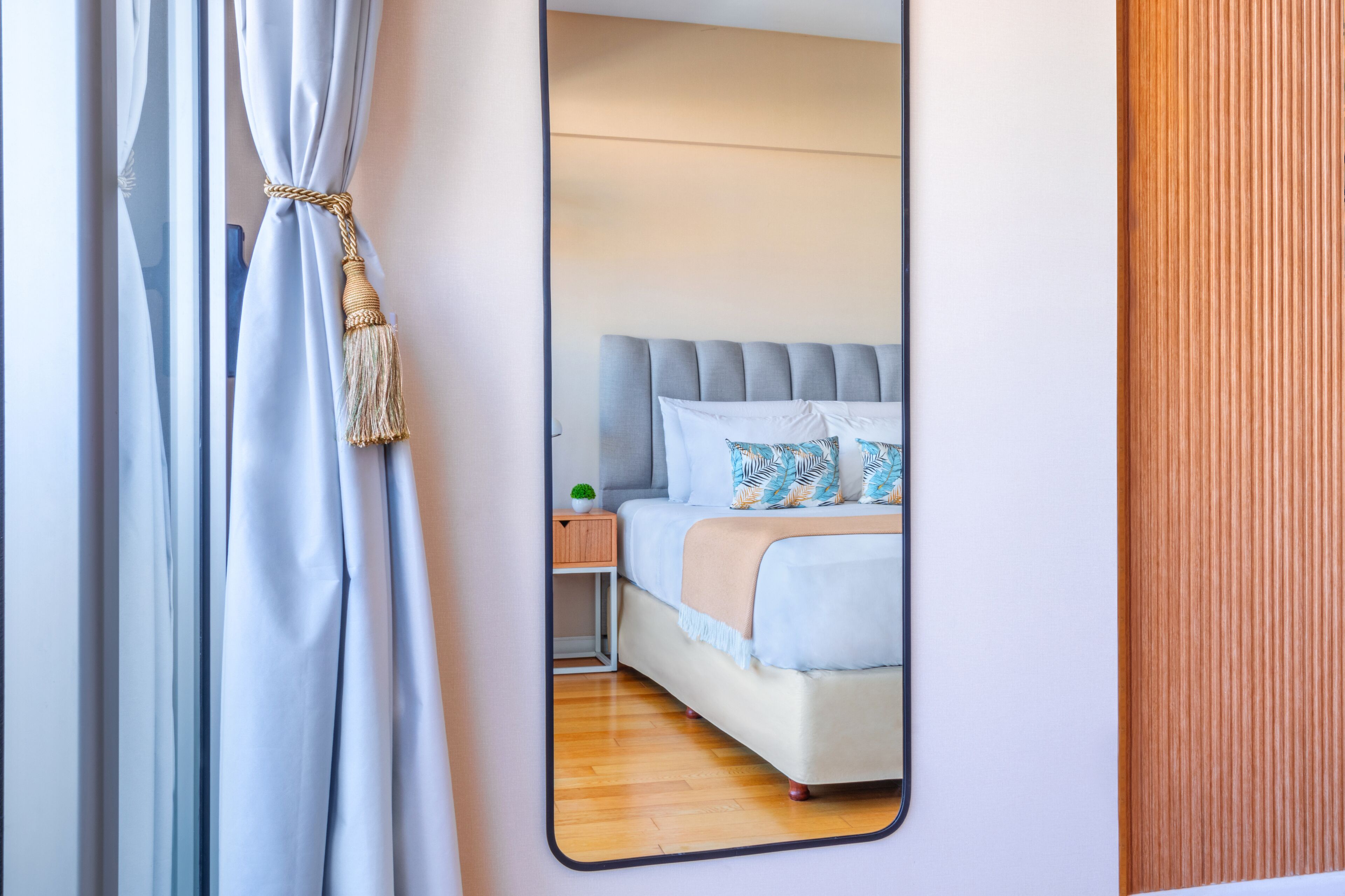 A bedroom with a bed, nightstand, and a mirror reflecting the room.