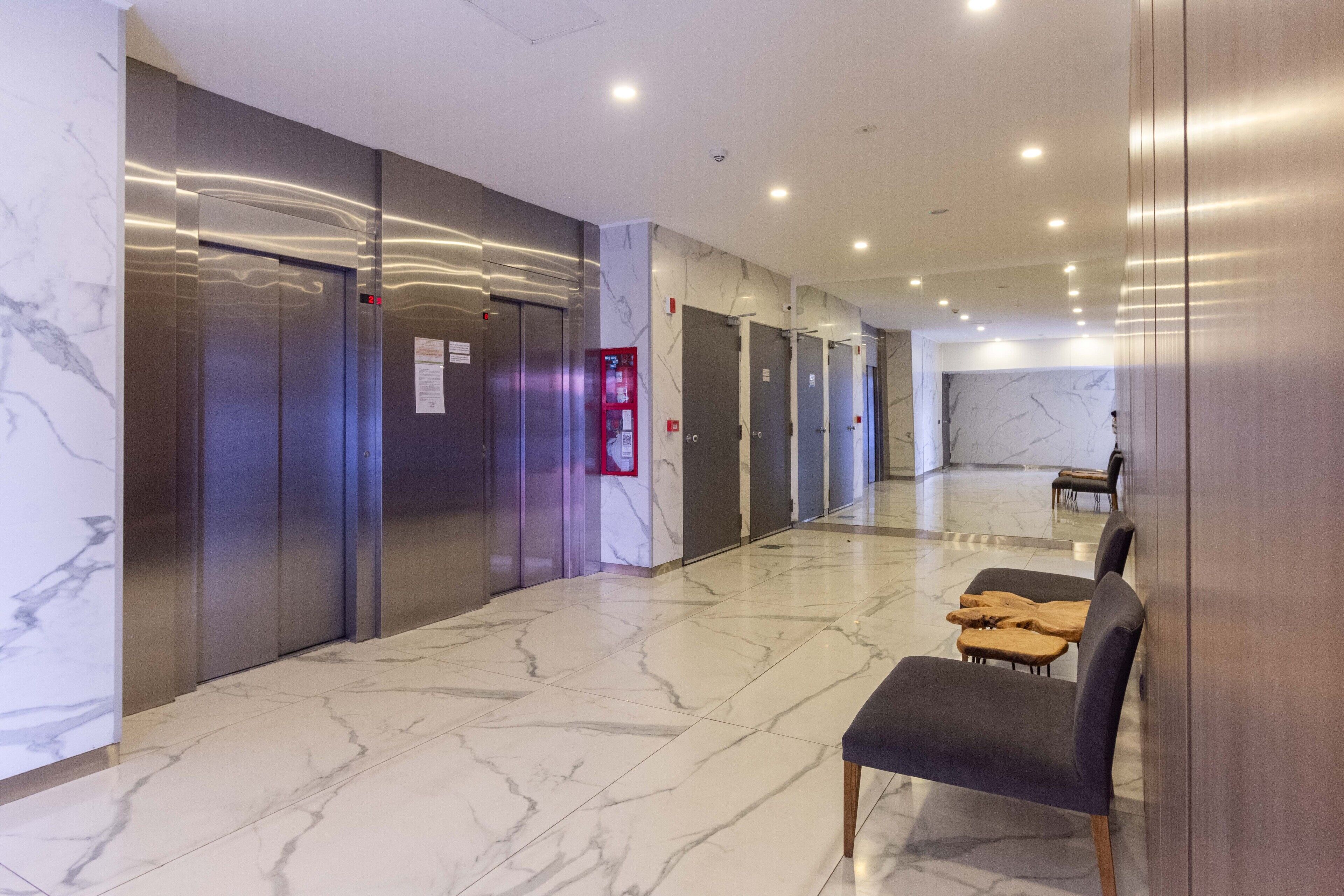 A hotel lobby with marble flooring, elevators, and a seating area with chairs.