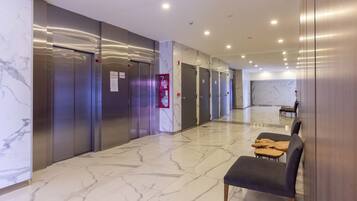 A hotel lobby with marble flooring, elevators, and a seating area with chairs.