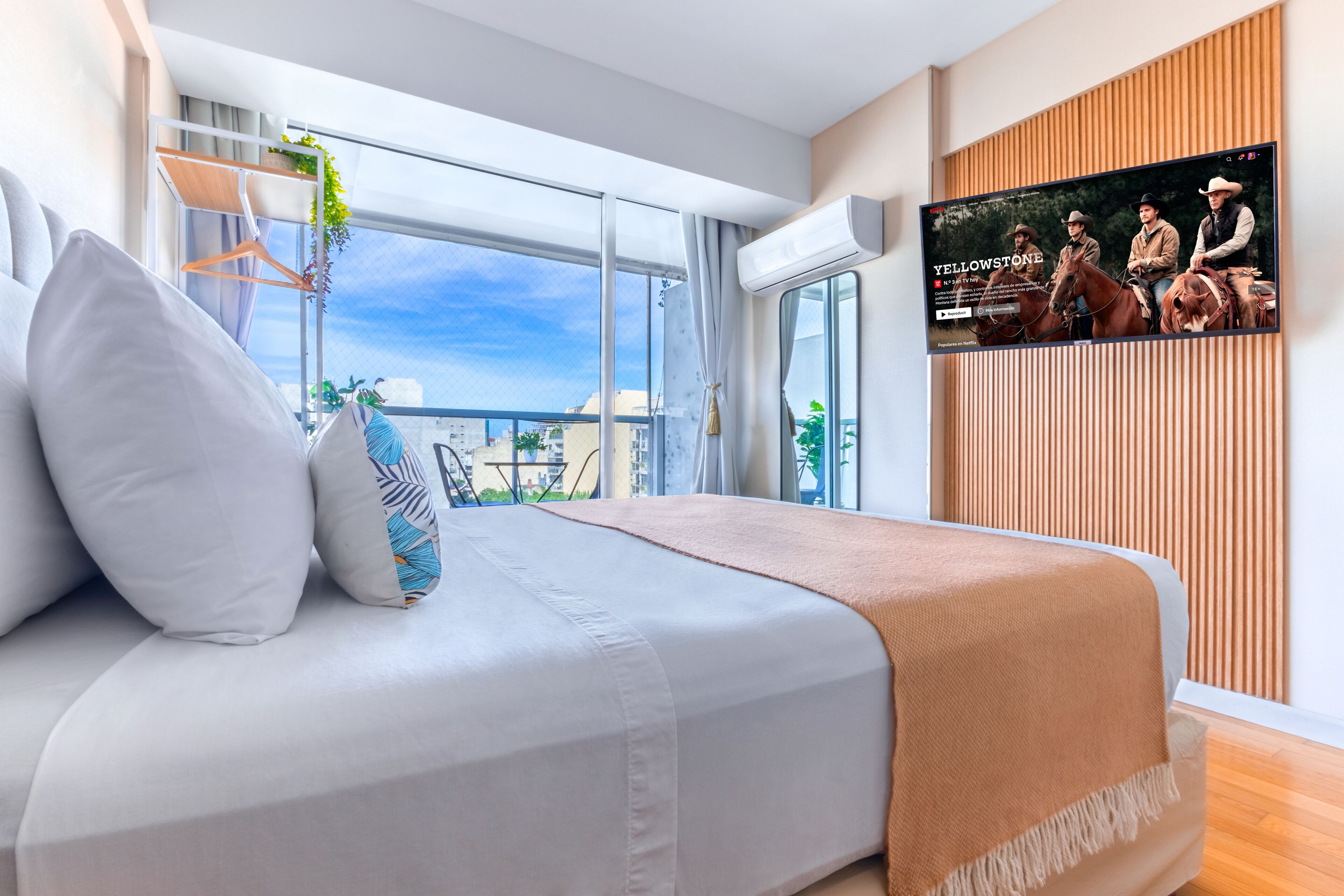 Habitación de hotel moderna con una cama grande, un televisor en la pared y vistas de la ciudad.