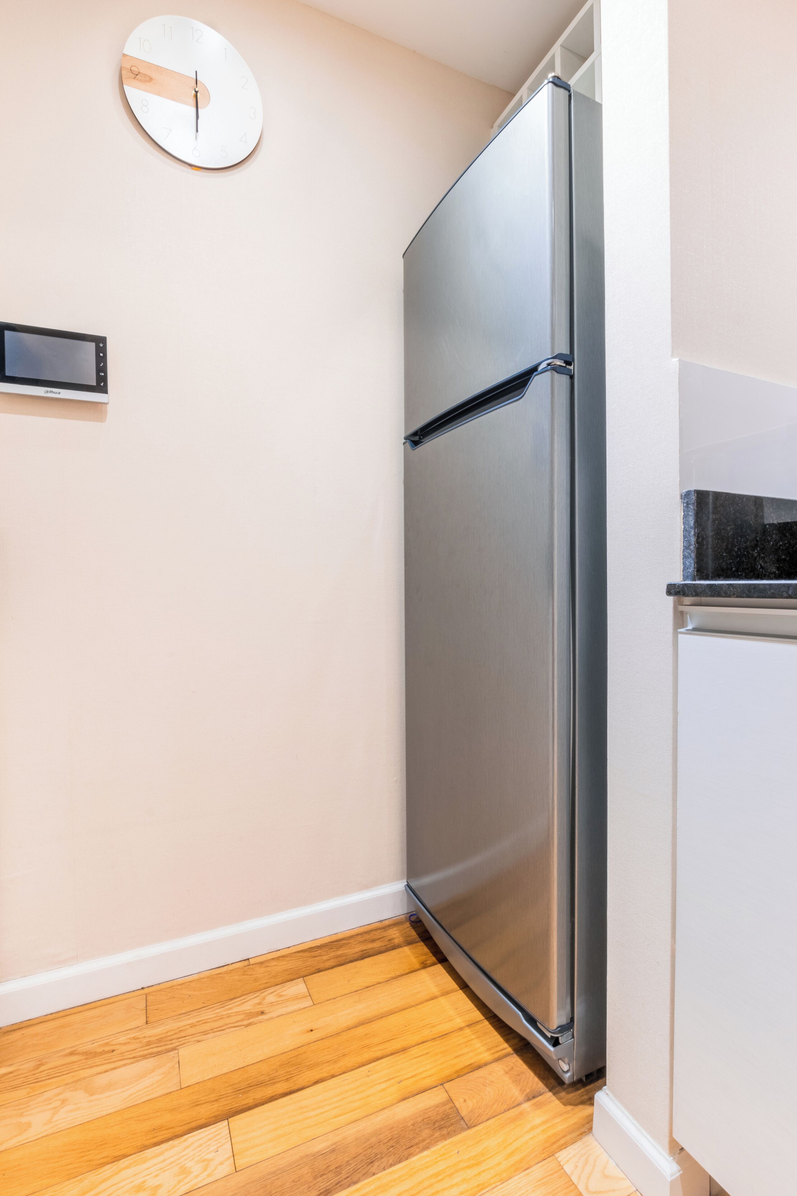 A kitchen with a stainless steel refrigerator, a wall clock, and a built-in oven.