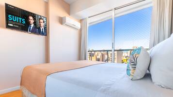 Hotelkamer met een groot bed, een aan de muur bevestigde televisie waarop een programma draait, en een stadszicht door het raam.
